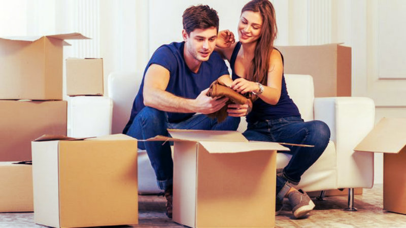 a couple sitting on a sofa while packing items in a cardboard box