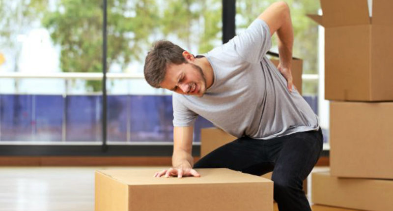 A man in pain while bending to pick up a heavy cardboard box