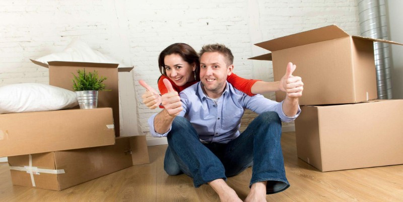 a man and woman sitting on floor alongside packed boxes