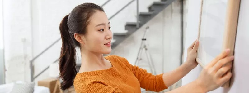 young beautiful woman hanging a photo frame on a wall