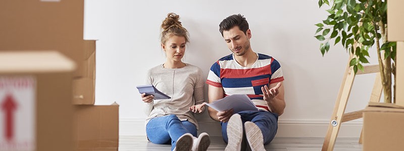 young couple sitting on the floor and calculating something using a calculator