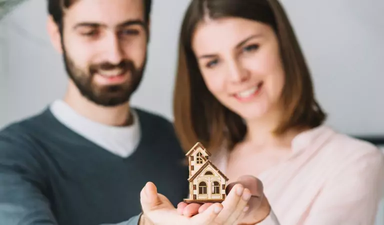 couple holding a dummy house on their hands
