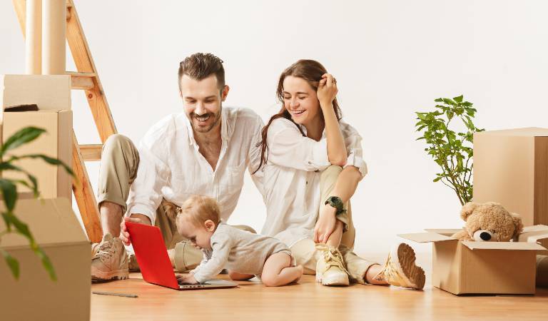 Couple is smiling and a new baby playing with a red laptop on the floor.